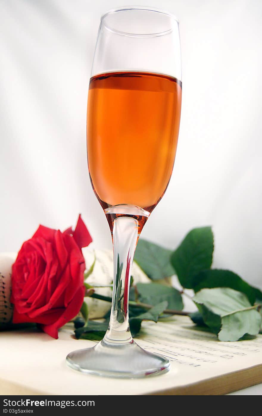 Red rose and champagne on a musical score background creating a romantic mood. Red rose and champagne on a musical score background creating a romantic mood.