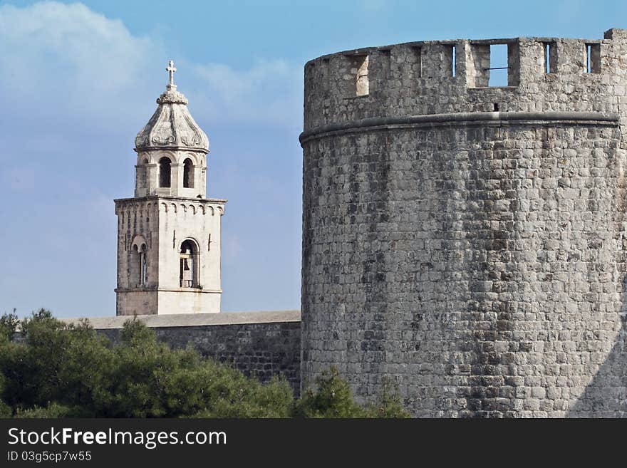 Church tower with imposing fortified stone wall and tower in the foreground. Possibilities for security and safety analogies or war and peace. Taken in Dubrovnik, Croatia.