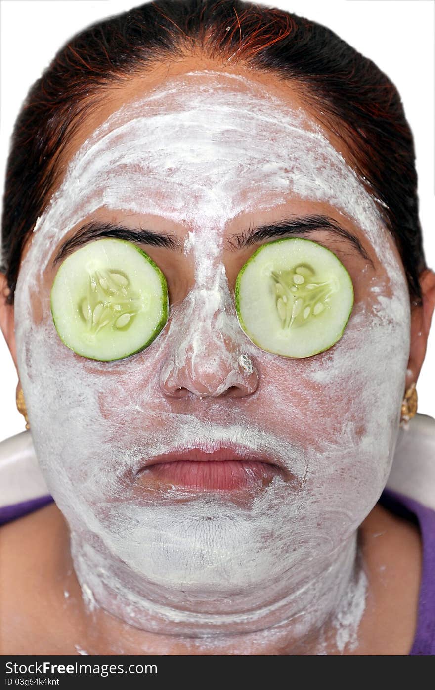 Lady applying a green cucumber face pack on his face.she is keeping cucumber slices on his eyes.it is good for face. Lady applying a green cucumber face pack on his face.she is keeping cucumber slices on his eyes.it is good for face.