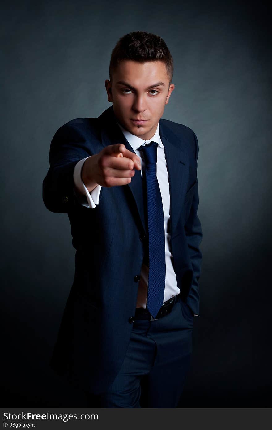 Fashion businessman pointing at the camera on a dark background