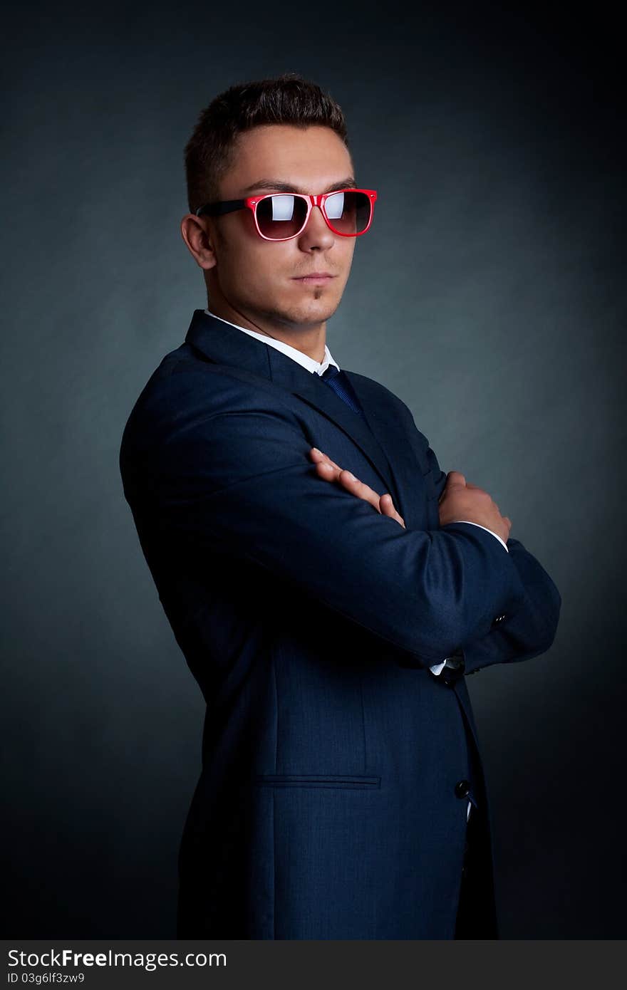 Confident fashion business man in red sunglasses standing with hands crossed