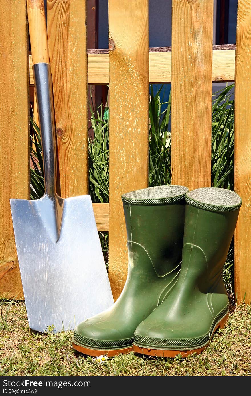 Rubber boots and spade in front of a brown fence