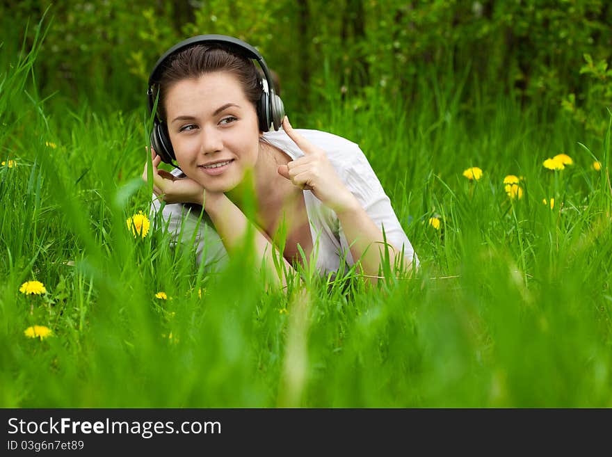 Pretty smiling woman listening musik on the grass and looking right, with space for text, background out of focus. Pretty smiling woman listening musik on the grass and looking right, with space for text, background out of focus