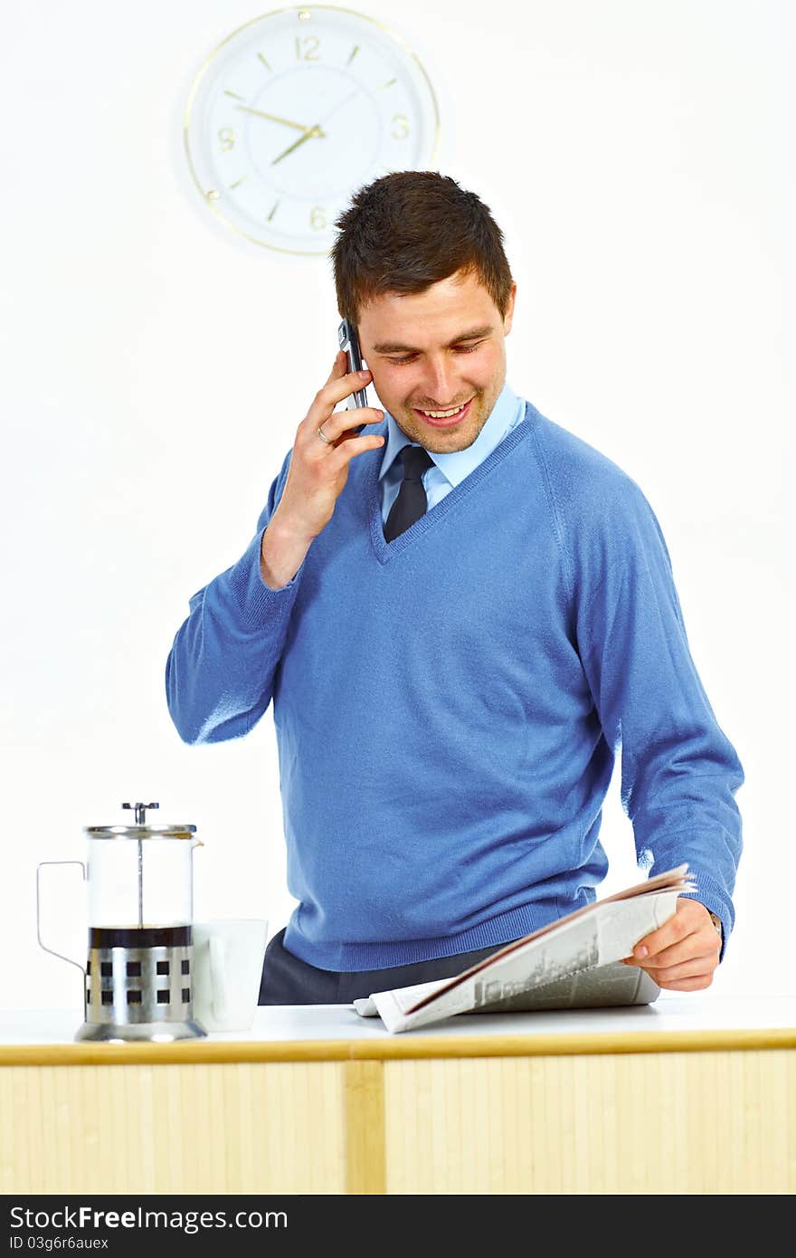 Businessman in kitchen talking by mobile phone, reading newspaper and smiling. Businessman in kitchen talking by mobile phone, reading newspaper and smiling