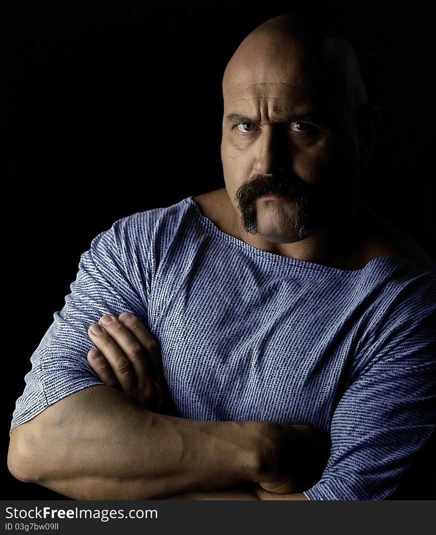 A bald headed body builder with arms crossed glaring at the camera