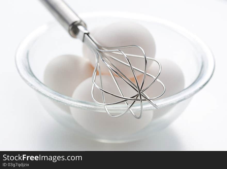 Metal whisk and fresh eggs in bowl, over white background.