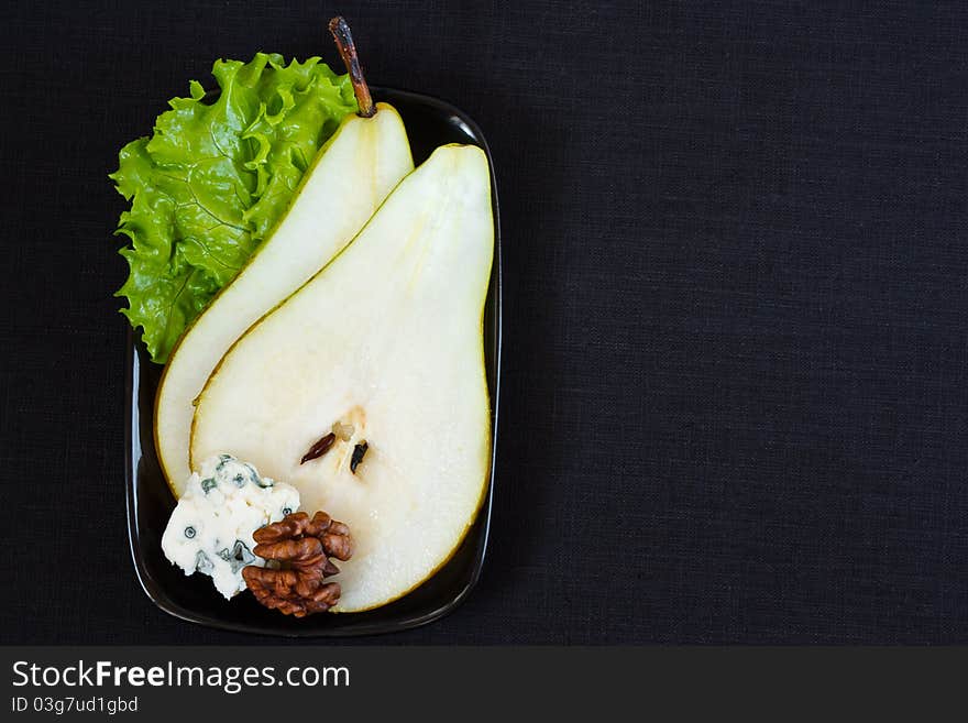 Pear with blue cheese, walnut and a leaf of green salad on a black background. Pear with blue cheese, walnut and a leaf of green salad on a black background.