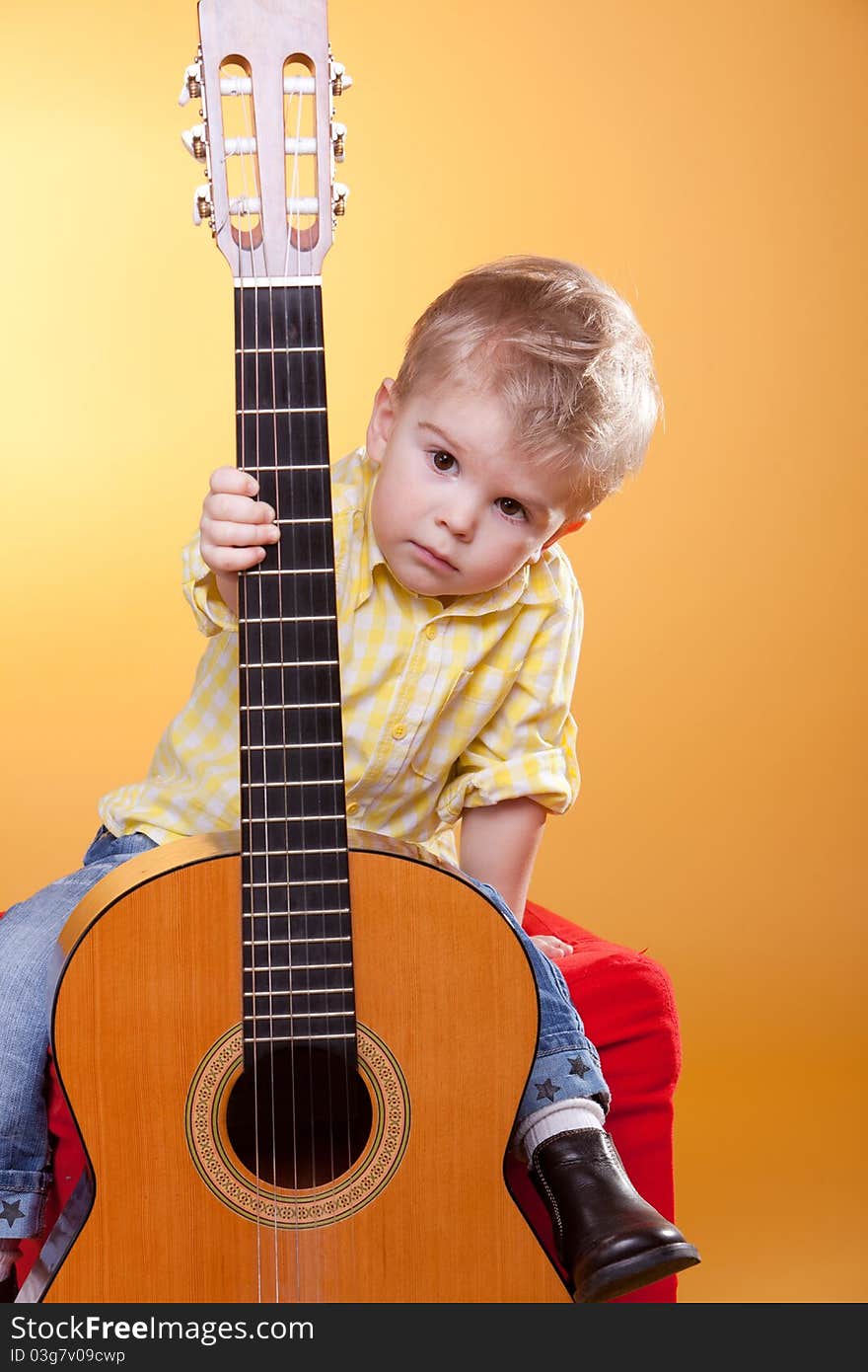 Child proposing play the guitar looking at camera