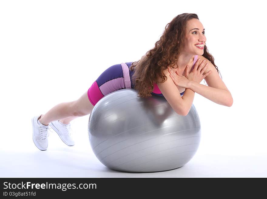 Beautiful brunette woman with big smile lying on top of fitness exercise ball for balance during workout. She is wearing bright blue and pink sports clothes and white trainers. Beautiful brunette woman with big smile lying on top of fitness exercise ball for balance during workout. She is wearing bright blue and pink sports clothes and white trainers.