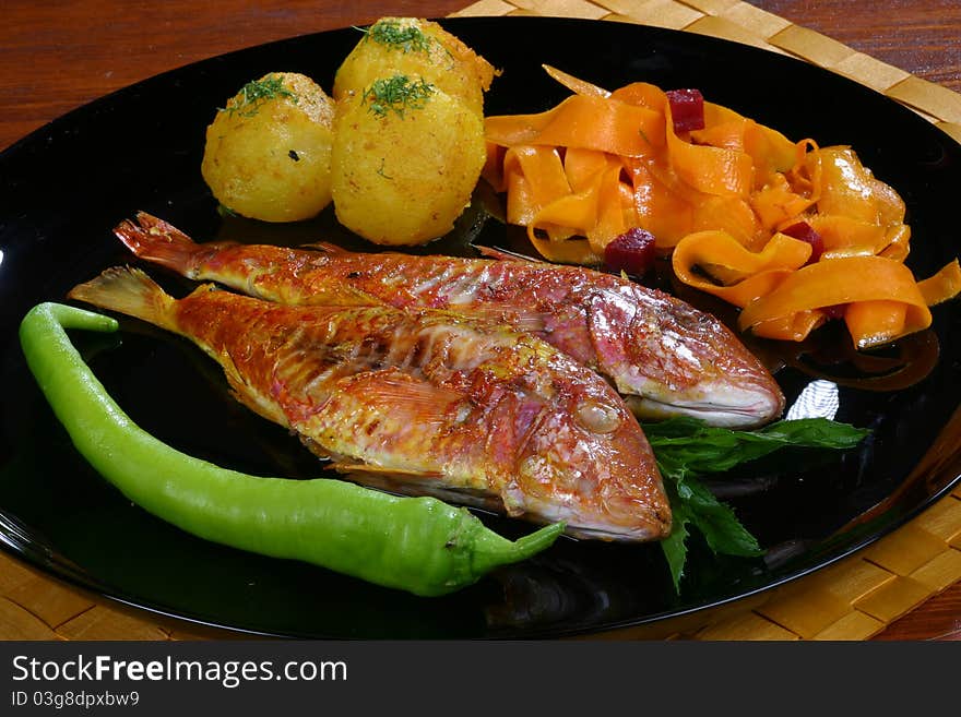 Fish with potatoes and pepper on a black plate