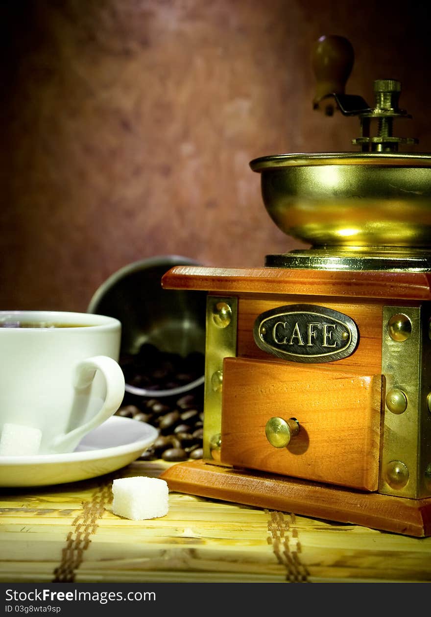 Cup full of coffee, beans, pot and grinder in night