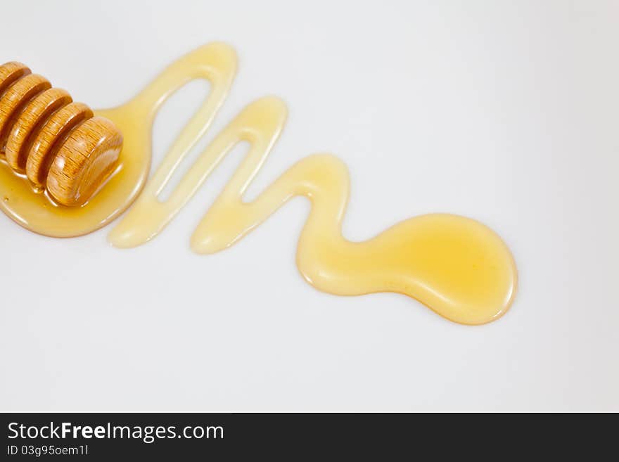 A honey dipper and a trail of honey on a neutral background. A honey dipper and a trail of honey on a neutral background.