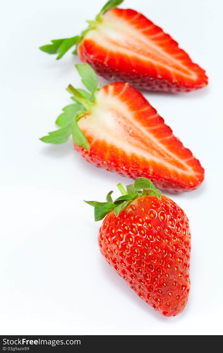 A whole strawberry in the foreground with a sliced strawberry in the background. A whole strawberry in the foreground with a sliced strawberry in the background.