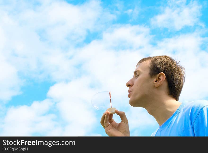 The young man starts up soap bubbles against the blue sky