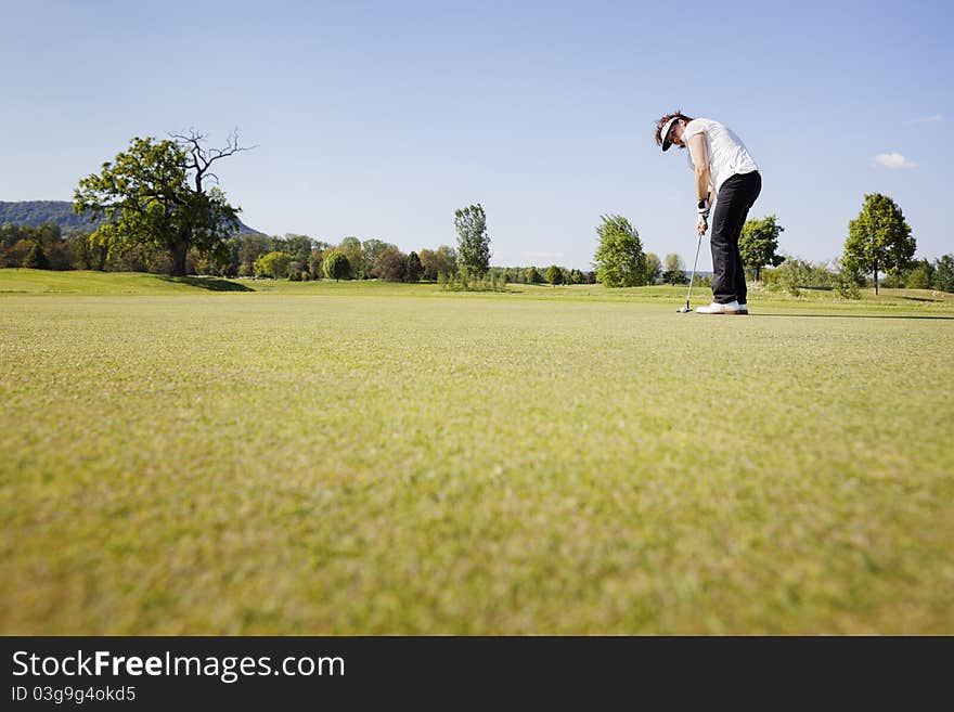 Active senior female golf player focusing for putting golf ball on green on beautiful golf course with blue sky in background. Active senior female golf player focusing for putting golf ball on green on beautiful golf course with blue sky in background.