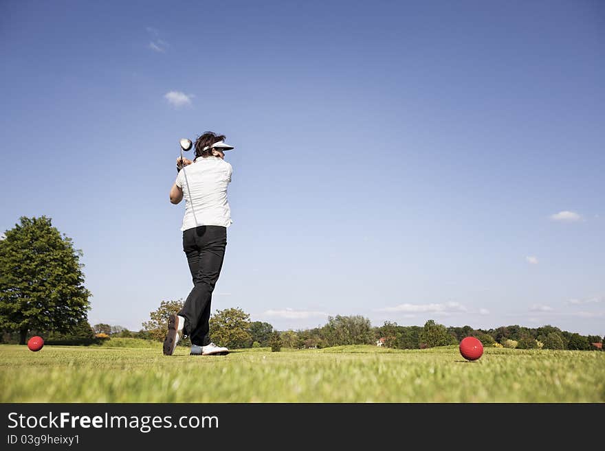 Active senior female golf player swinging golf club to tee off ball on beautiful golf course with blue sky in background. Active senior female golf player swinging golf club to tee off ball on beautiful golf course with blue sky in background.