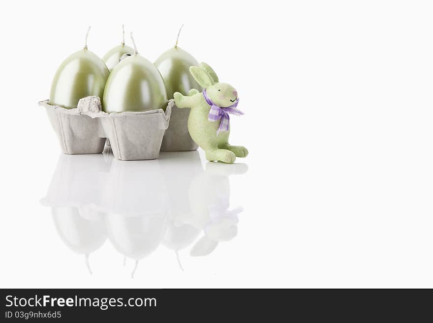 A green easter-bunny and four easter-candles on white background