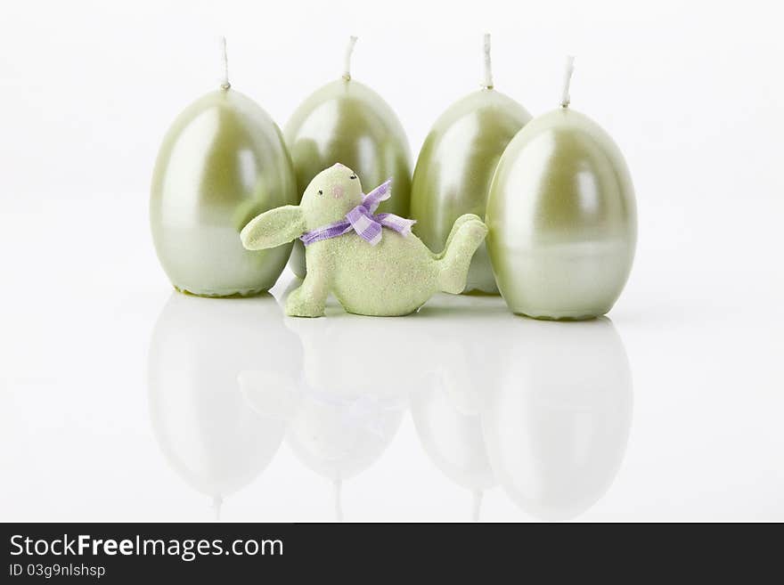 A green easter-bunny and four easter-candles on white background