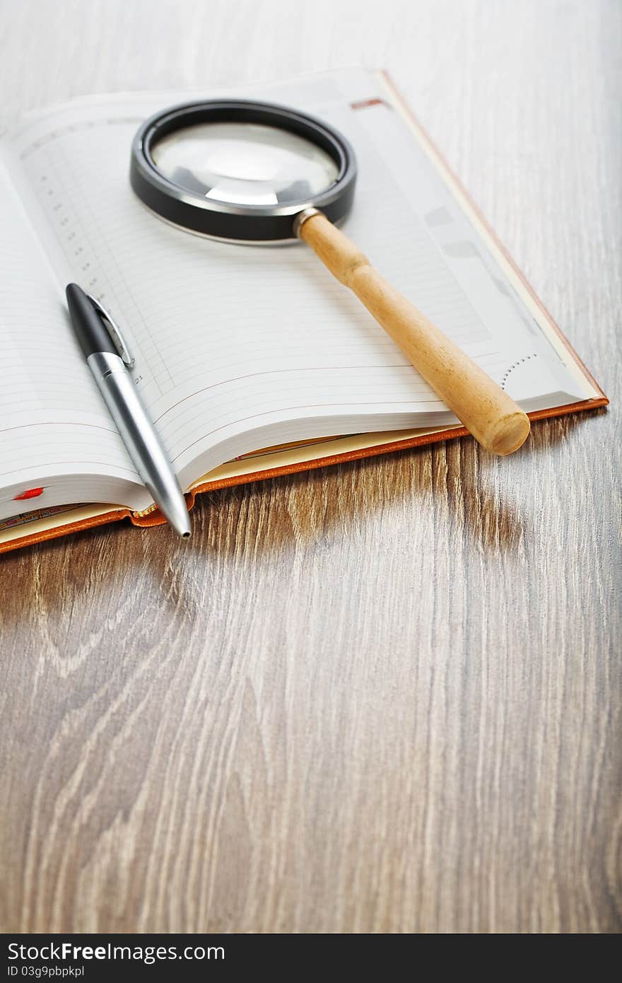 Studio shot composition of office or education accessories pen and magnifying glass on notebook on wooden board