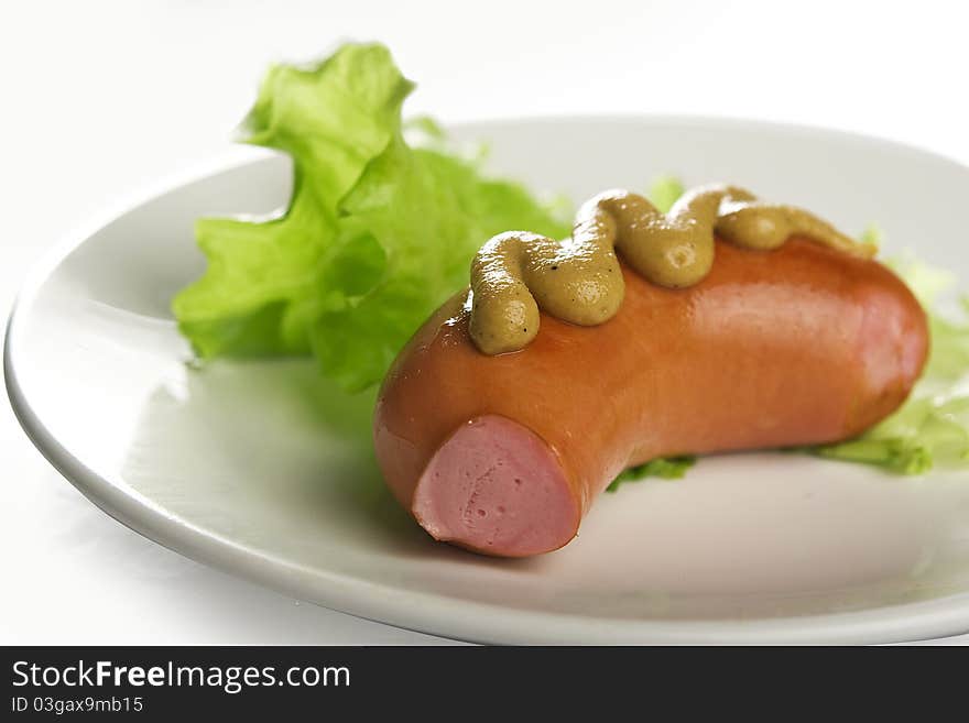 Small sausage with mustard and lettuce on the plate