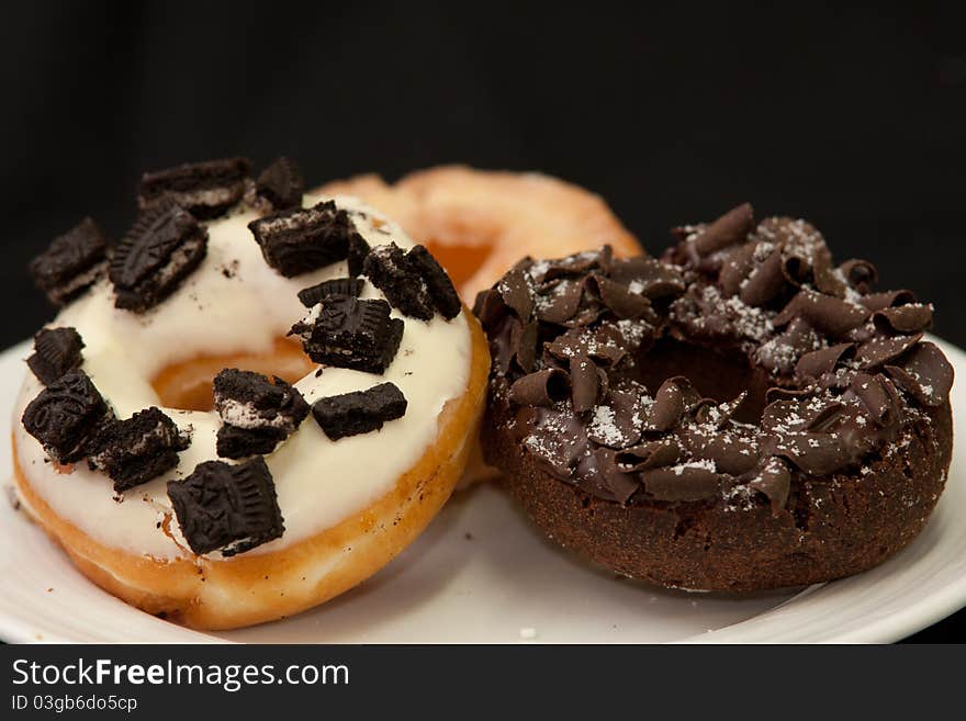 The white chocolate topping with olio and chocolate donut in white dish and dark isolated backgrond. The white chocolate topping with olio and chocolate donut in white dish and dark isolated backgrond