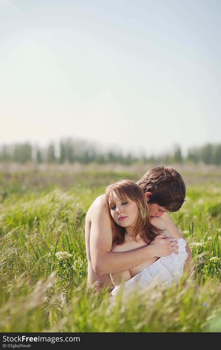 Beautiful young pair kissing and hugging on green grass