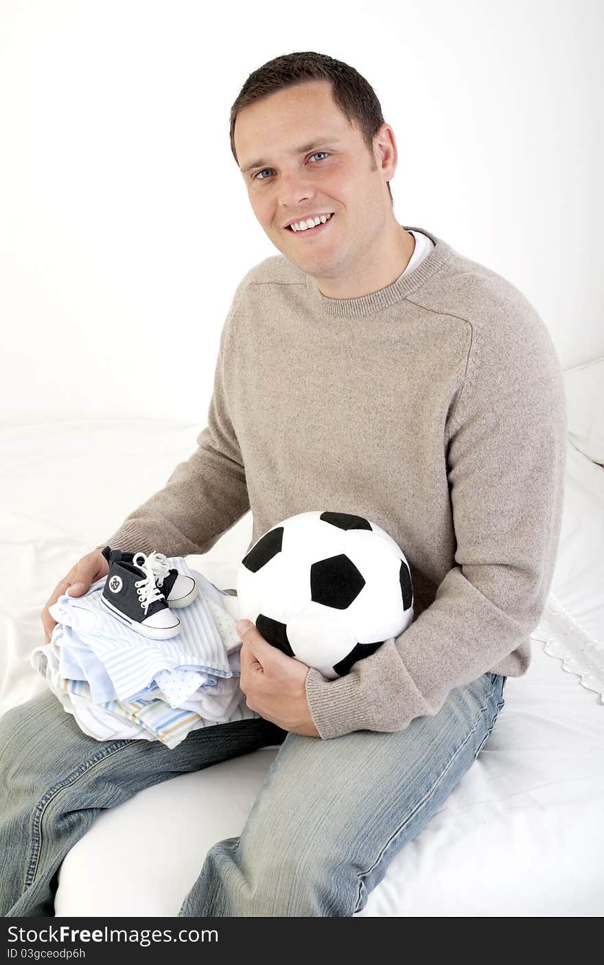 Man looking to camera holding baby boy clothes and football - baby son. Man looking to camera holding baby boy clothes and football - baby son