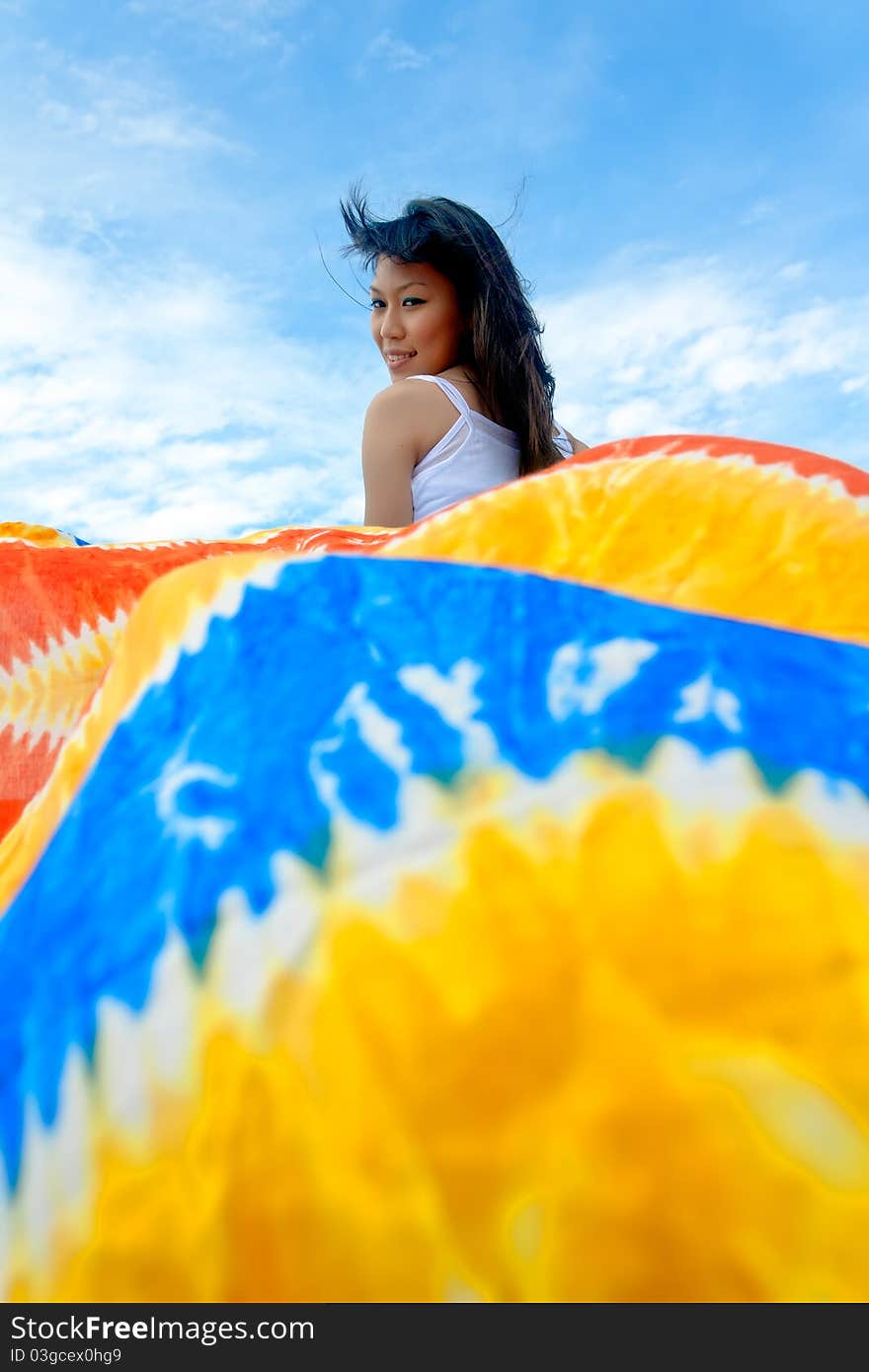 Pretty young sensuality girl is holding colorful batik sarong in front of moving boat during holiday