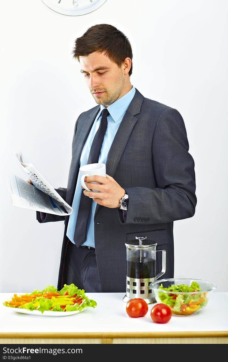 Businessman with cup of coffee reading newspaper in the kitchen. Businessman with cup of coffee reading newspaper in the kitchen