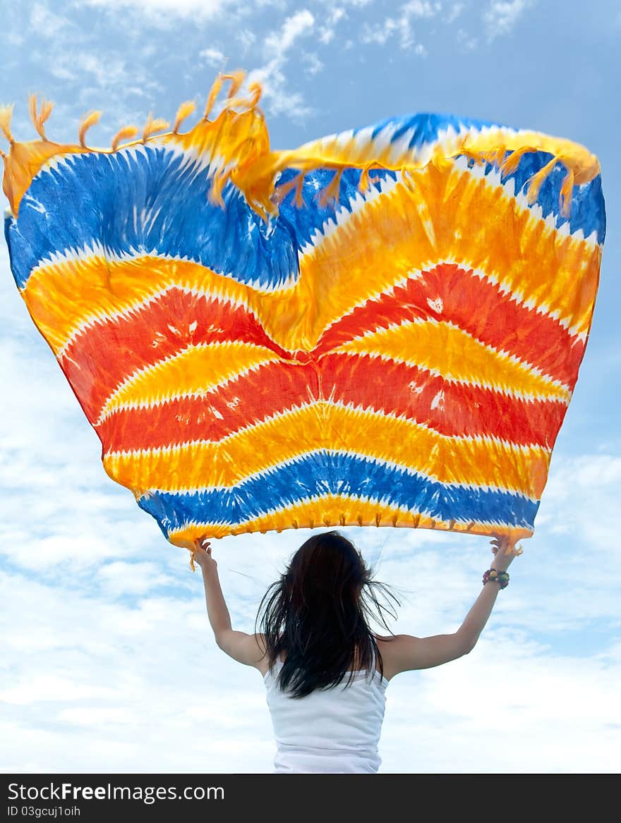 Pretty young sensuality girl is holding colorful batik sarong in front of moving boat during holiday