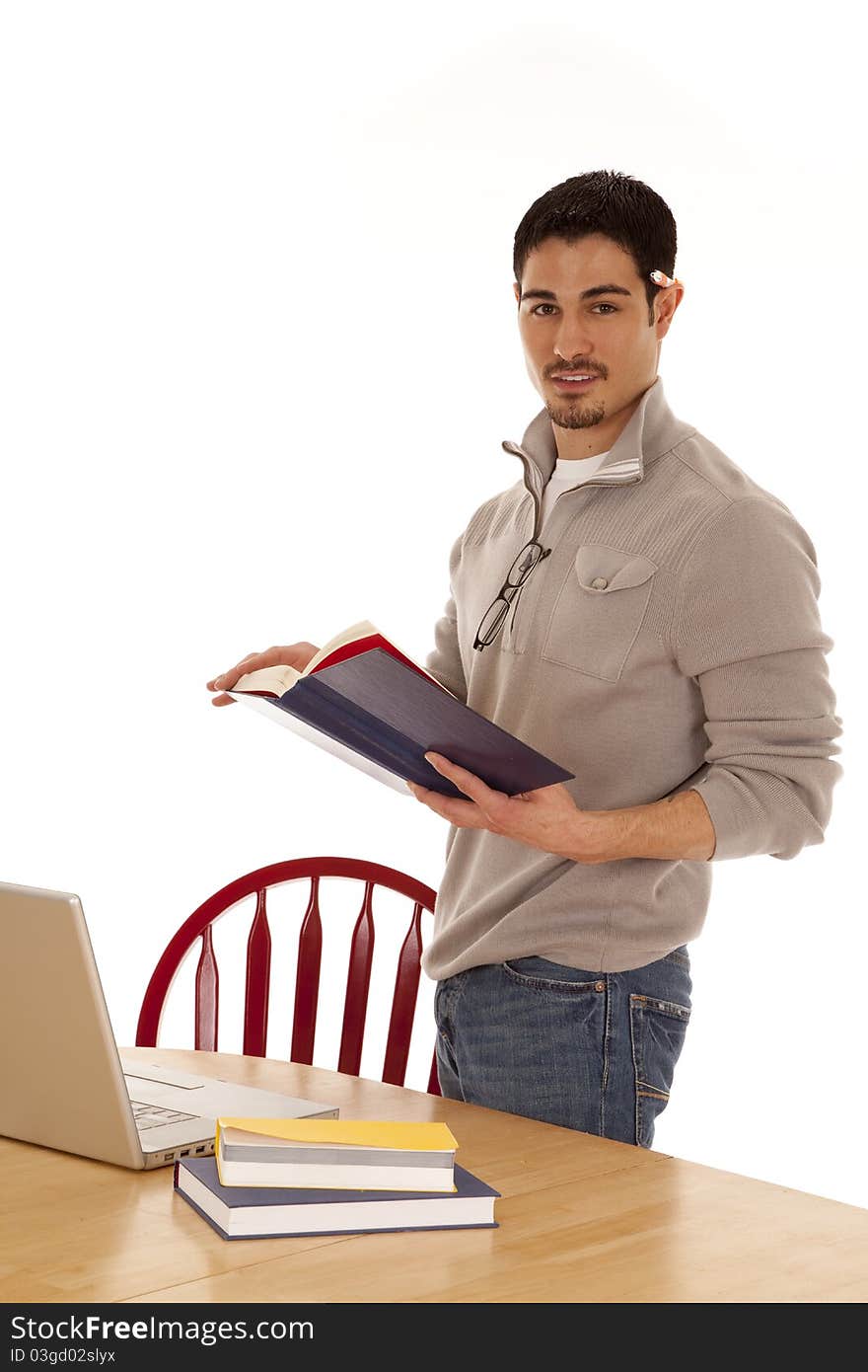 A man is standing by a table with a book and a laptop. A man is standing by a table with a book and a laptop.