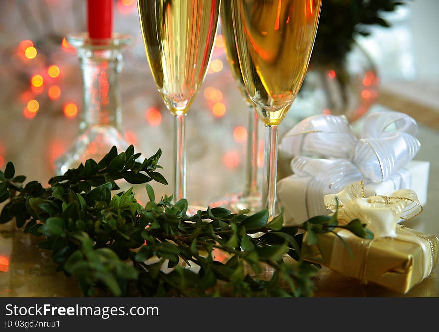 Champagne in glasses, green twig, gift boxes and blured lights on background. Champagne in glasses, green twig, gift boxes and blured lights on background.