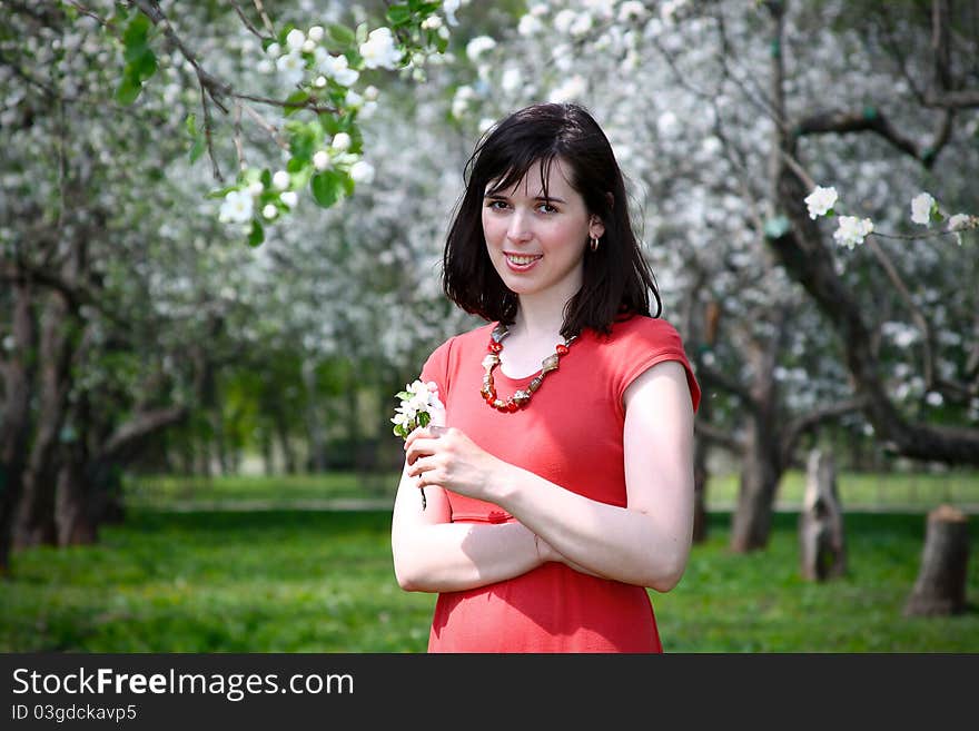 Girl in a red dress with a sprig of apple in his hands against the backdrop of flowering trees