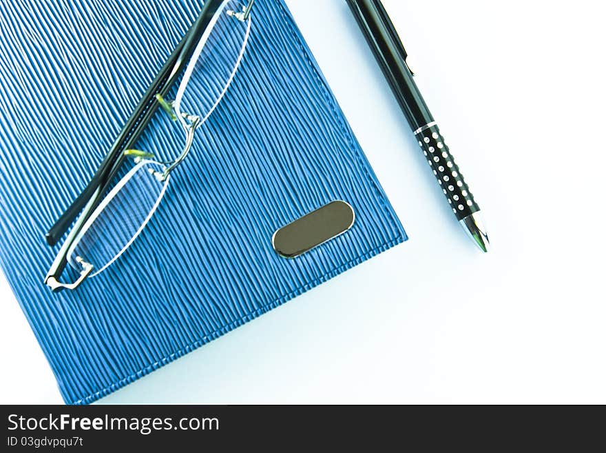 Glasses on blue notebook with black pen in isolation. Glasses on blue notebook with black pen in isolation