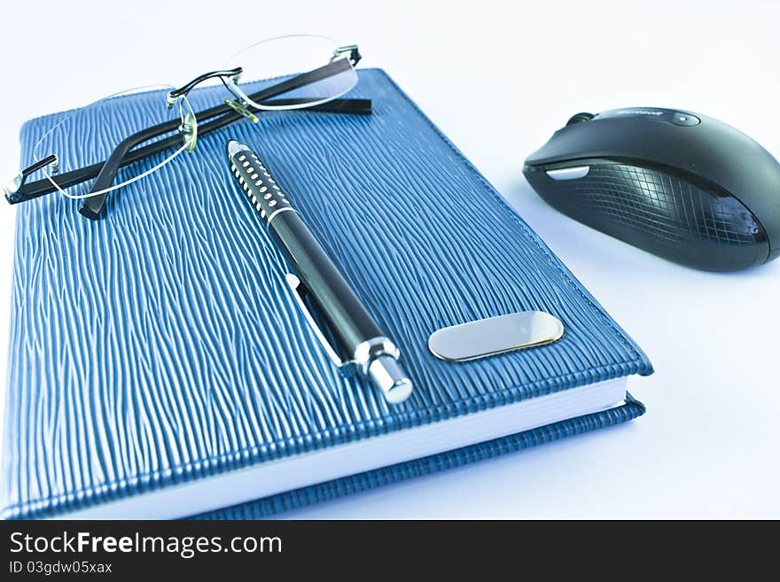 Glasses on blue notebook with black pen and mouse in isolation. Glasses on blue notebook with black pen and mouse in isolation