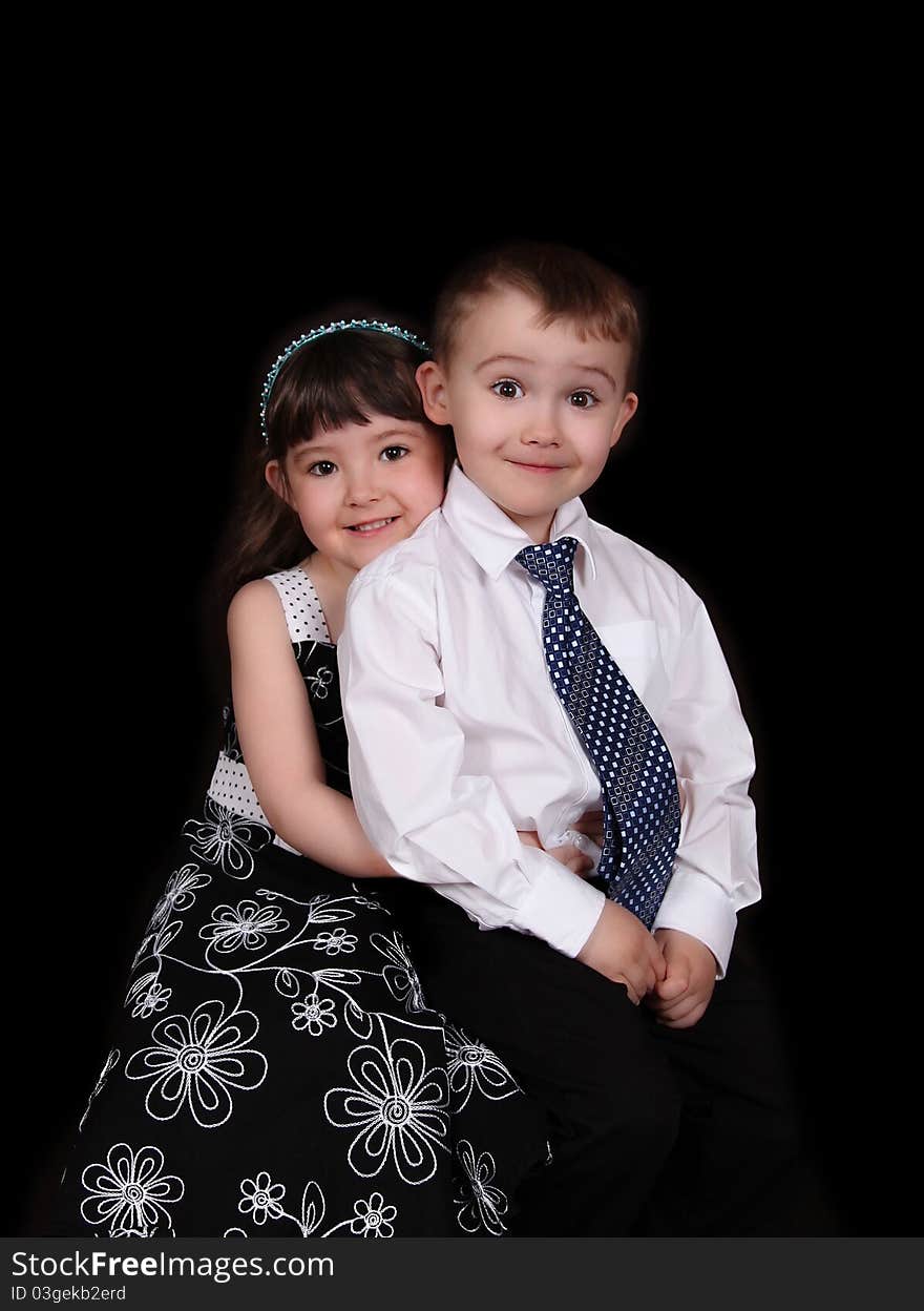 Adorable portrait of young brother and sister sitting and embracing. isolated on black. Adorable portrait of young brother and sister sitting and embracing. isolated on black