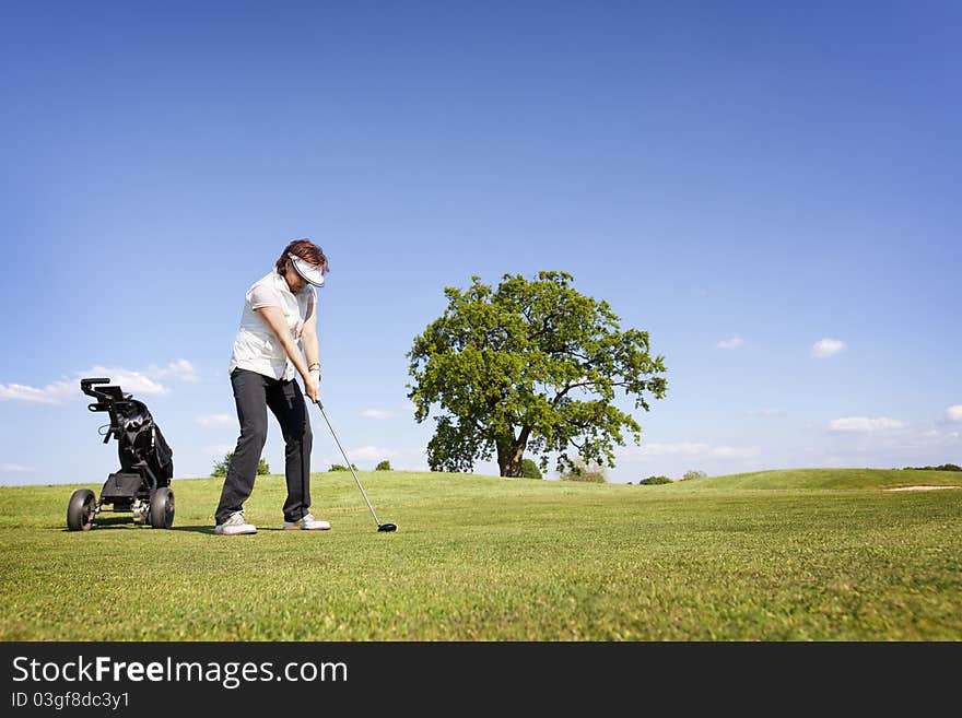 Active senior female golf player with golf bag concentrating to hit the ball with driver on fairway on beautiful golf course with blue sky in background. Active senior female golf player with golf bag concentrating to hit the ball with driver on fairway on beautiful golf course with blue sky in background.