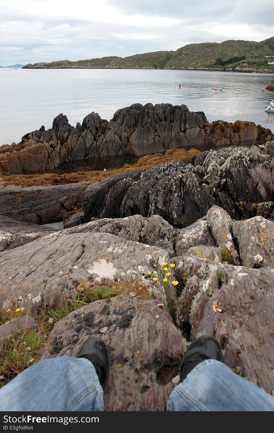 A lone hiker on the edge of the coast of kerry in ireland watching kayakers. A lone hiker on the edge of the coast of kerry in ireland watching kayakers