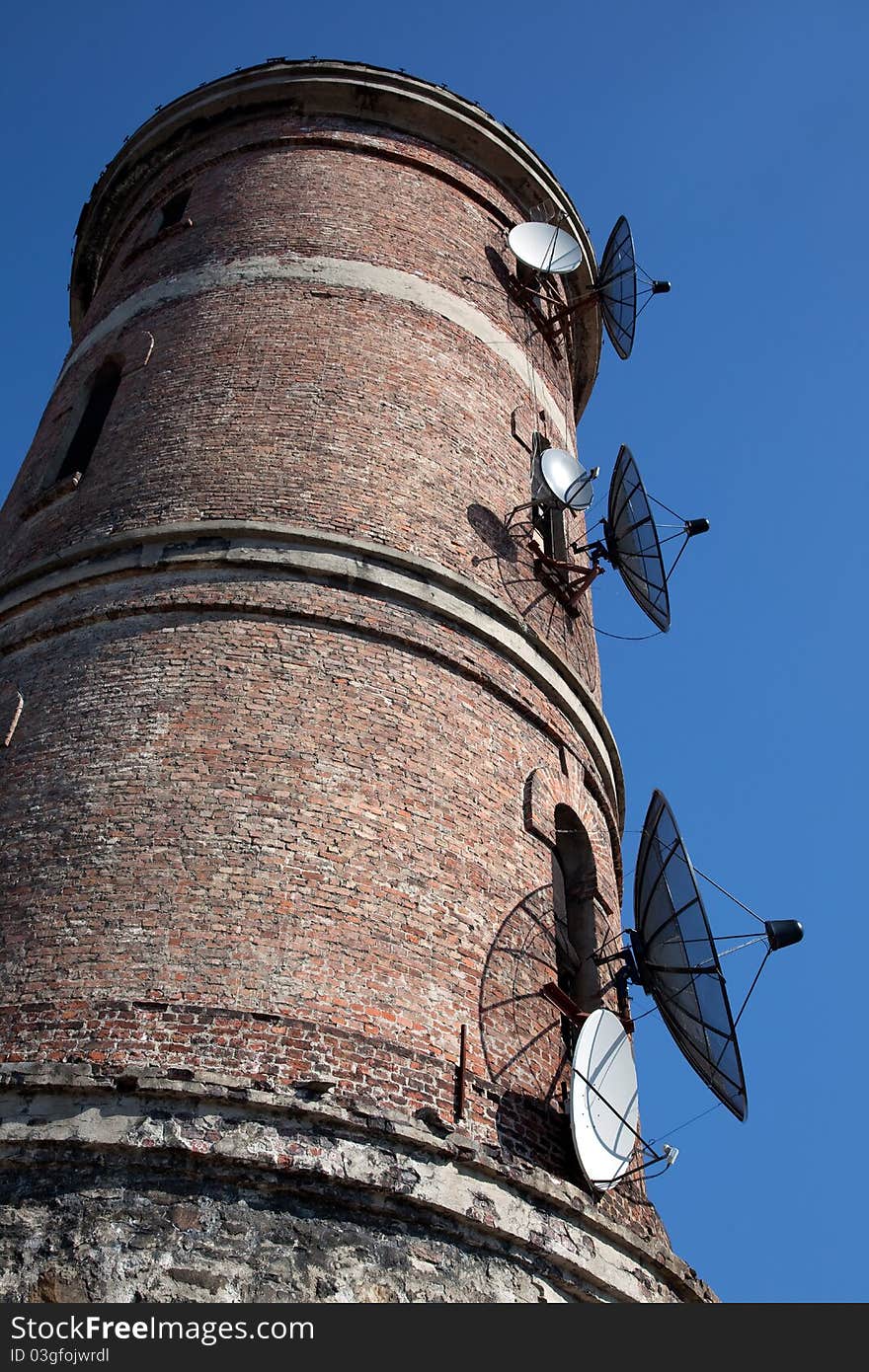 Modern communications antenna on an old tower against the blue sky