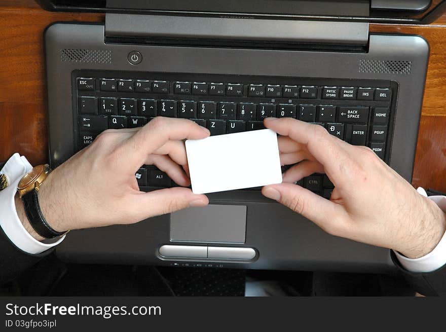 Businessman holding blank business card with laptop on background