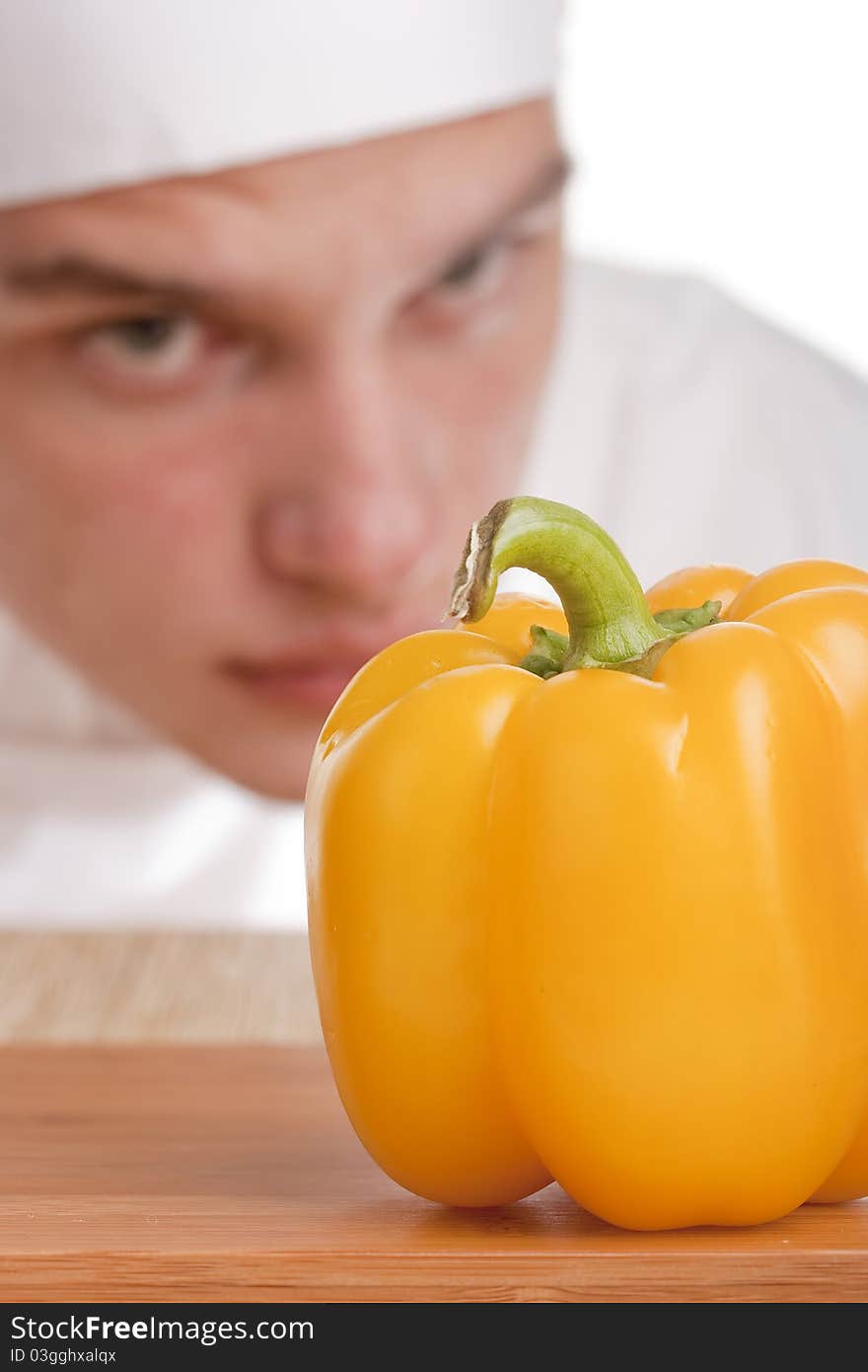 The young chef in chef's hat is considering a pepper. The young chef in chef's hat is considering a pepper.