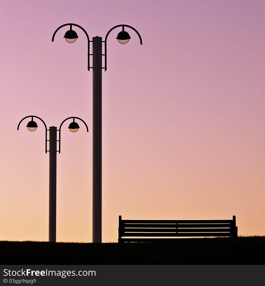 Silhouette of empty bench and streetlamps against a beautiful evening pink sky. Silhouette of empty bench and streetlamps against a beautiful evening pink sky