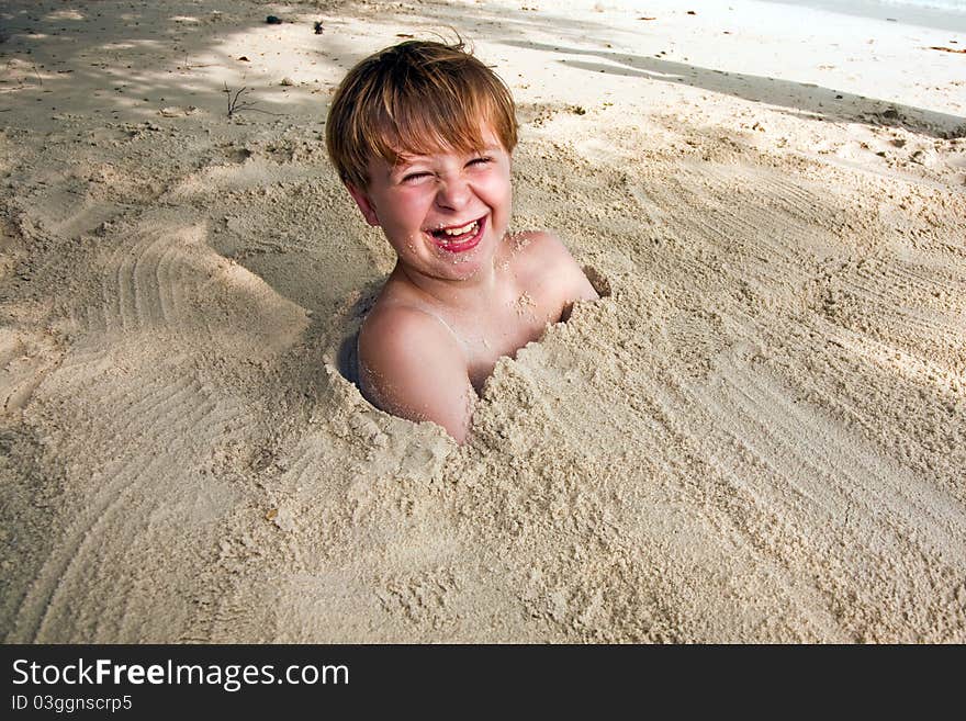 Happy young boy covered by fine sand at the beach