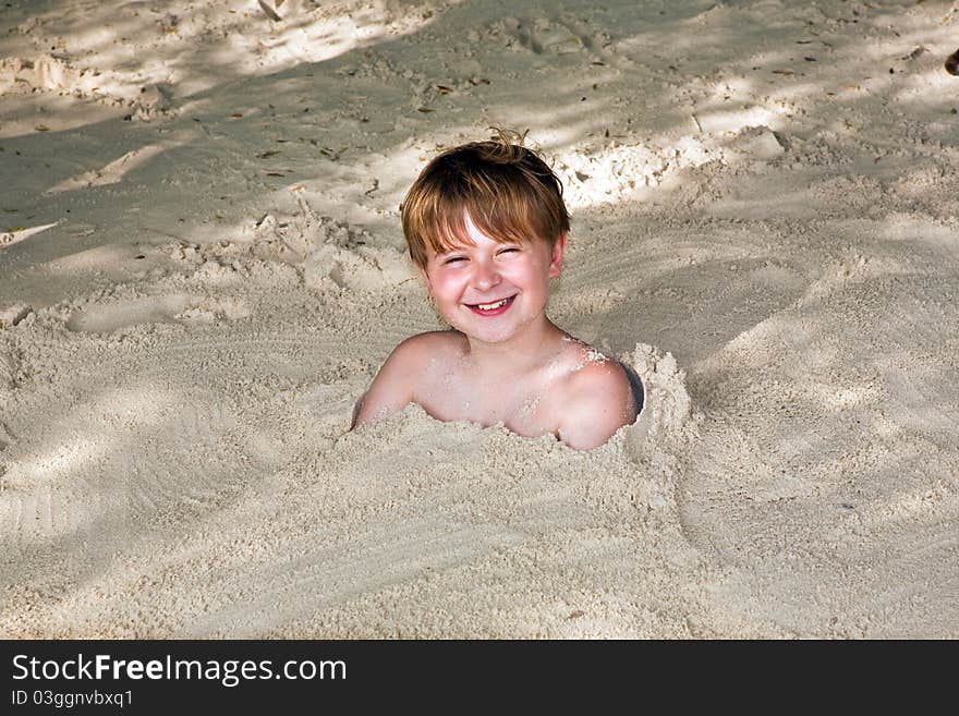 Happy young boy covered by fine sand at the beach