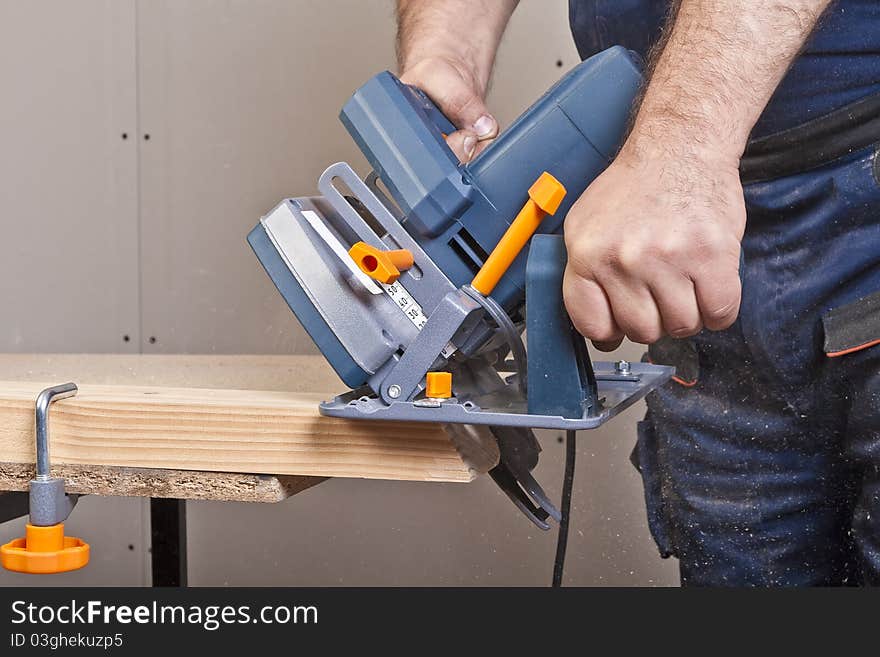 Close-up of a construction worker's hand and power tool while planing a piece of wood trim for a project. Close-up of a construction worker's hand and power tool while planing a piece of wood trim for a project.