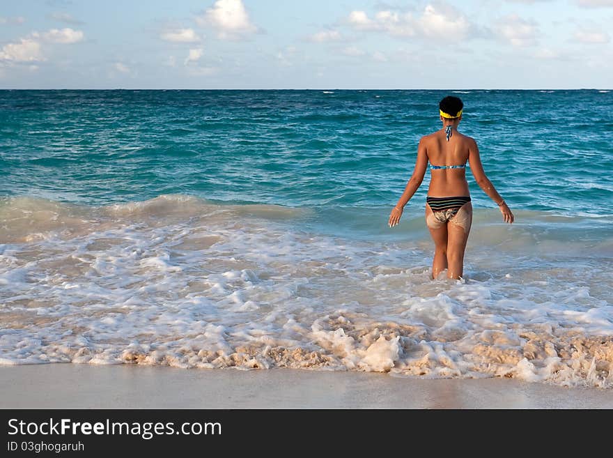 Tanned girls is standing in bright blue ocean under blue sky