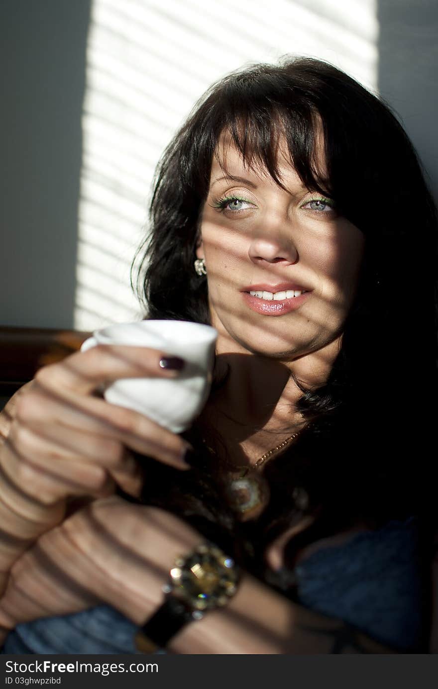 Girl with a cup of coffee poses at the window with shutters