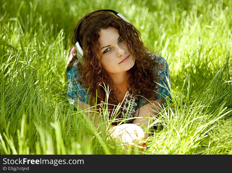 Redhead girl with headphone at green grass