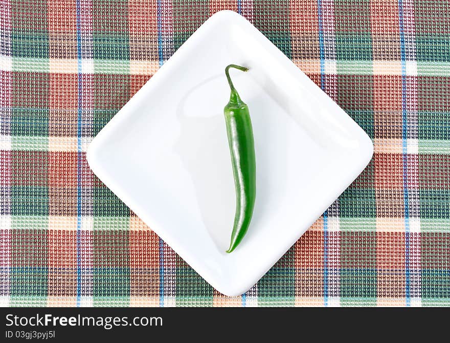 One green chili pepper on a white plate and checkered placemat