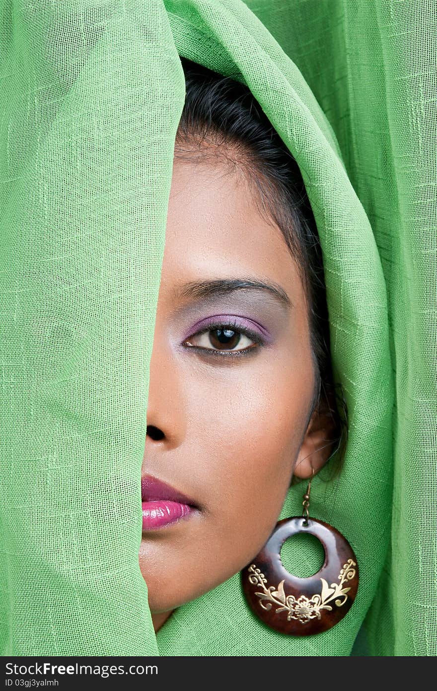 Beautiful woman of east indian descent looks from behind a green curtain. Beautiful woman of east indian descent looks from behind a green curtain